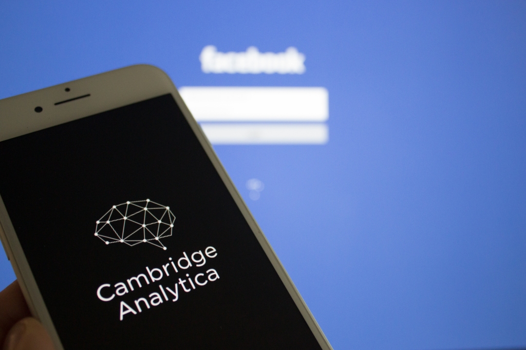 A scary looking Cambridge Analytica app in front of blurred out Facebook login screen
